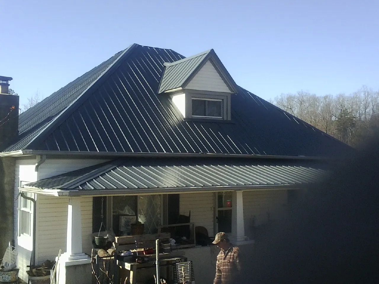 Dark blue standing seam metal roof with a dormer above a front porch in Oil City