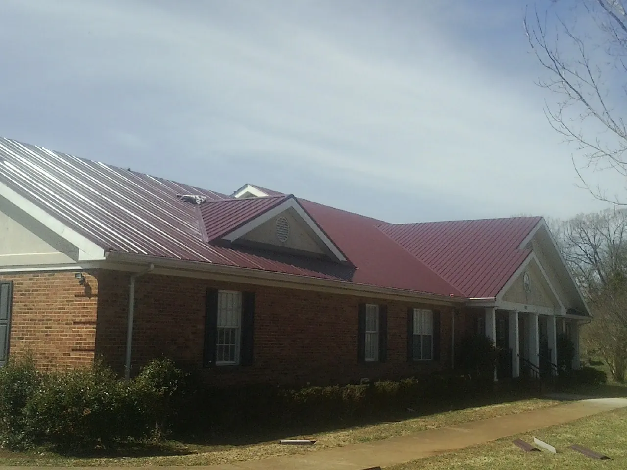 Red metal roof with gabled entries on a long brick building, from a Hail Damage Roof Repair job in Oil City