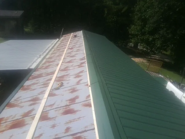 Old rusted panels beside newly installed green metal roofing — Wind Damage Roof Repair by Roofing Brothers in Oil City