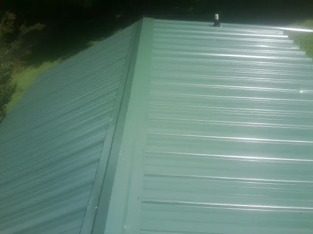 New green metal panels meeting at the ridge of a roof — Flat Roof Repair work by our crew in Oil City
