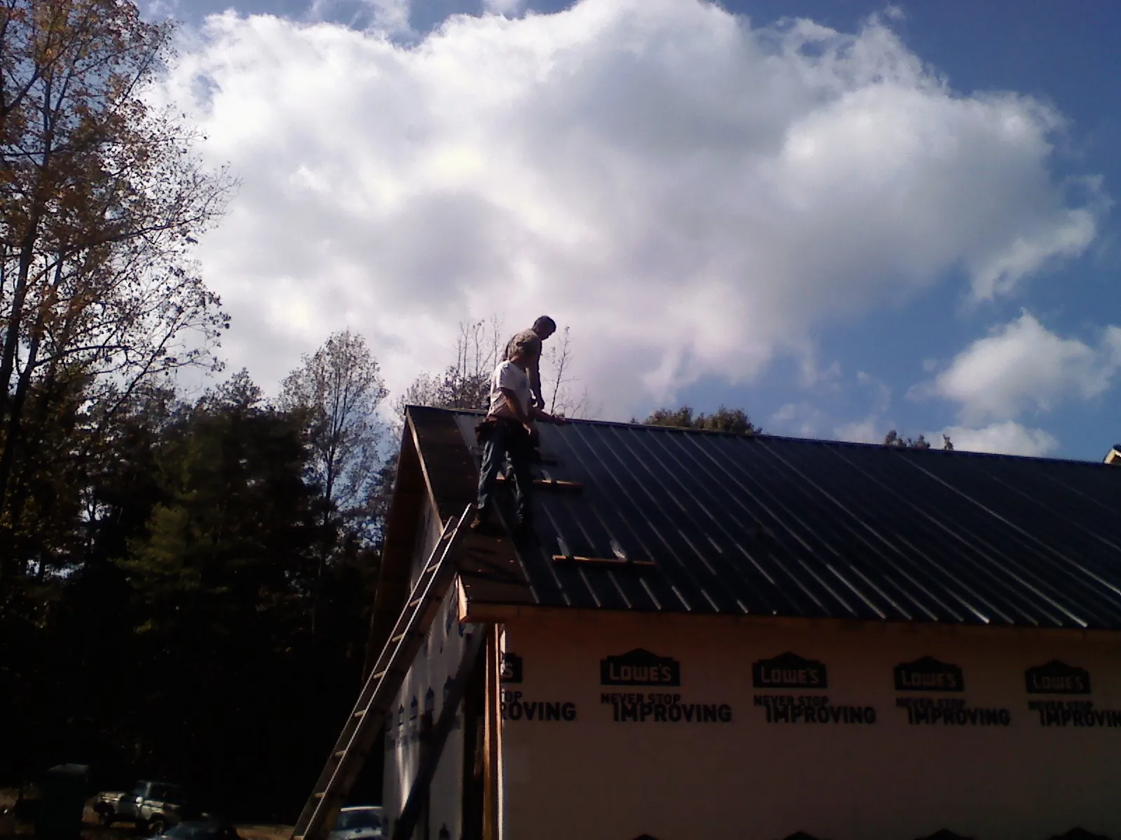 Roofer fastening dark metal panels high against a cloudy sky, from a Roof Inspection job in Oil City