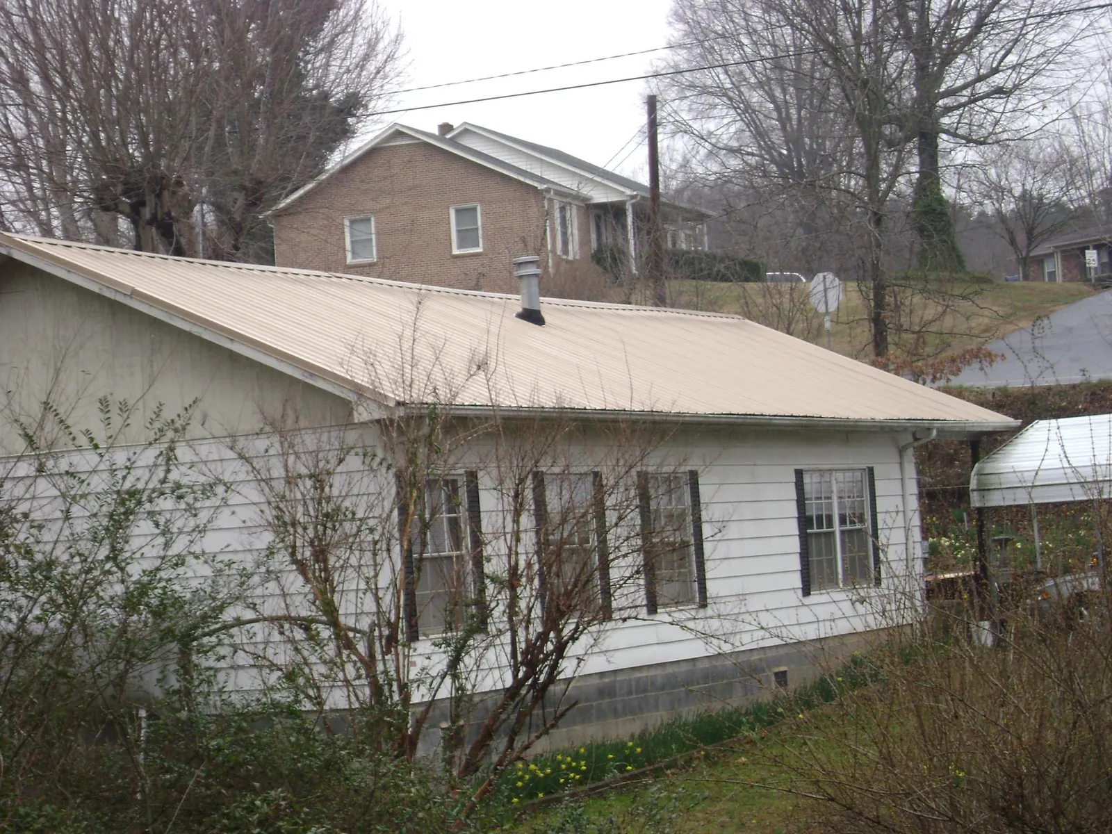 Tan metal roof on a white sided house set into a hillside — Commercial Roofing by Roofing Brothers in Oil City
