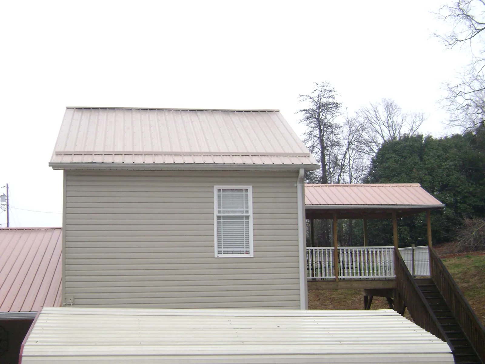 Tan metal roofs on a two story addition and attached porch, from a Roof Replacement job in Oil City
